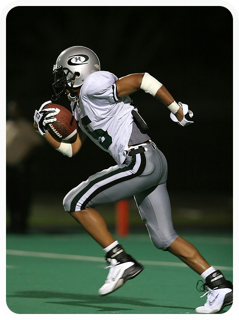 American football player in white and gray uniform running with the ball on a field at night.